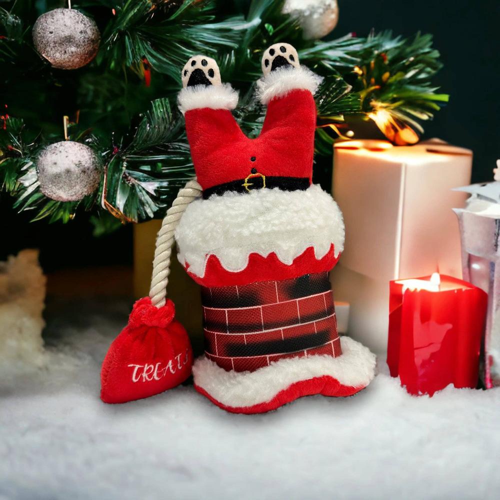 A festive Christmas-themed dog toy featuring Santa Claus stuck in a chimney under a christmas tree